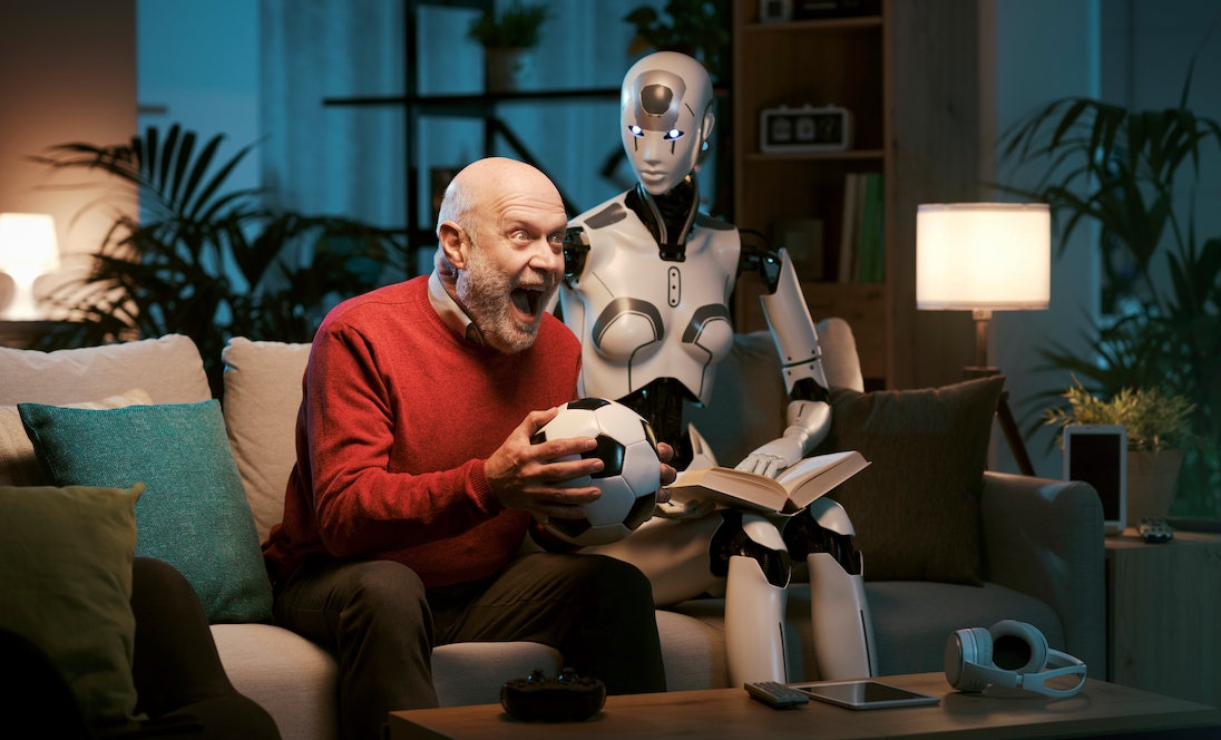 oudere man op sofa met voetbal in zijn hand en naast hem een robot